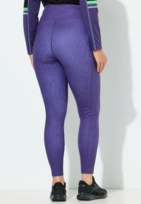 Fialové legíny s texturovaným vzorem zebry, vybavené vysokým pasem a doplněné černými sportovními botami.