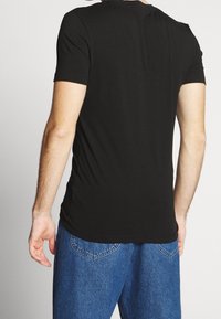 Camiseta negra ajustada, de manga corta, con textura suave y cuello redondo, combinada con vaqueros de mezclilla azules, mostrando un diseño simple y limpio.