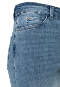 Close-up van lichtblauwe spijkerbroek met zichtbare voorzak, klein muntenzakje met metalen klinknagel, riemlussen en gedetailleerde stiksels.