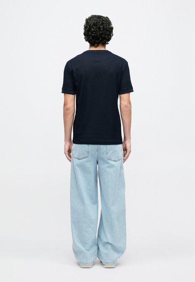 Μπλε ναυτικό βαμβακερό T-shirt με κοντά μανίκια και ίσια άκρη, συνδυασμένο με ανοιχτό γαλάζιο τζην φαρδιάς γραμμής και λευκά αθλητικά παπούτσια.