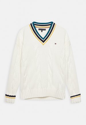 Pull en laine blanche à mailles torsadées avec un col en V rayé de teal, noir et jaune, et des poignets rayés assortis, arborant un petit logo de drapeau sur la poitrine.