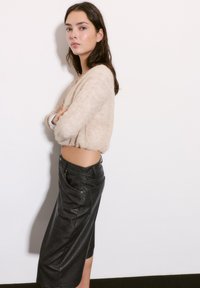 Pulover texturat, bej, cu mâneci bufante, asociat cu o fustă din piele neagră, ajustată, până la genunchi, dotată cu buzunare și cusături vizibile.