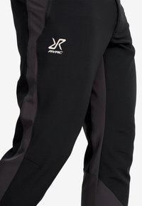 Svarta träningsbyxor med en texturerad tyg, kontrasterande mörkgrå sidopaneler och en liten vit logotyp på vänster lår.