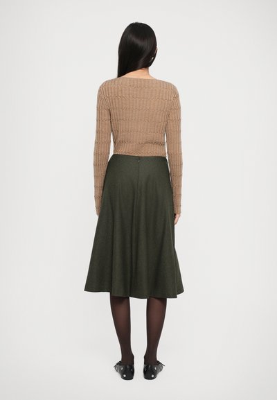 Pulover din tricot maro, cu model în relief și mâneci lungi, împreună cu o fustă A-line verde închis, până la genunchi, purtat cu încălțăminte neagră și dresuri.