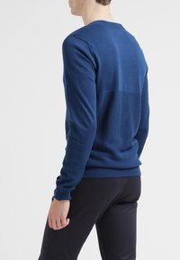 Marinblå stickad tröja med rund hals, med ett strukturerat mönster på baksidan, ribbade muddar och fåll. Lämplig för lager-på-lager-styling.