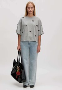 Graues T-Shirt mit kurzen Ärmeln und schwarzen Schleifendetails, kombiniert mit hellblauen weiten Jeans und einer großen schwarzen Tote-Tasche mit einem dekorativen Schlüsselanhänger.