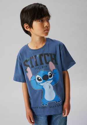 Boy wearing blue t-shirt featuring animated character Stitch flexing arms with text "STITCH" and "KEEP GOING - KEEP GROWING."