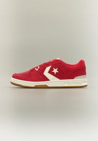 Basket Converse basse rouge avec logo étoile blanche et chevron, semelle intermédiaire blanche et semelle extérieure en caoutchouc naturel, vue de profil.