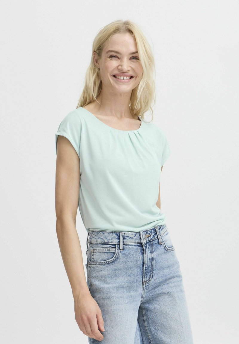 Haut vert menthe à manches courtes avec un col rond et des plis subtils, associé à un jean en denim bleu clair à taille haute.