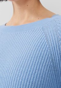Pull en tricot bleu clair avec un motif de côtes texturé, présentant un décolleté large et des manches courtes. Matière douce et respirante.
