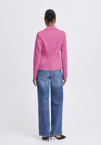 Figurbetonter rosa Blazer mit Kerbkragen, kombiniert mit hochtaillierten, weit geschnittenen Jeans aus Denim. Das Jackett verfügt über Schulterpolster und Rückennähte.