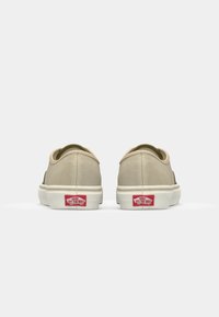 Pantofi sport din pânză bej cu design low-top, talpă din cauciuc albă și logo roșu pe călcâi. Textură netedă cu detalii minime.