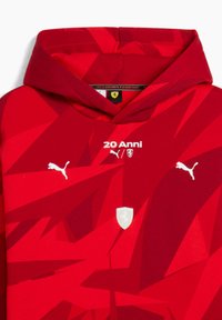 Felpa con cappuccio rossa con motivo geometrico in tonalità di rosso più scure, logo Puma bianco, scritta "20 Anni" ed emblema Ferrari sul petto.