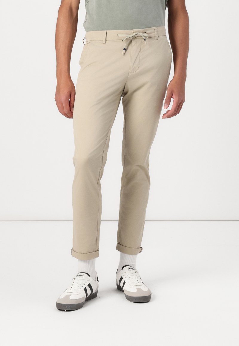 Beige chinos med snor i taljen, slim fit, opsmøgede kanter og frontlommer, parret med hvide og grå sneakers.