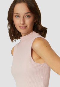 T-shirt sans manches côtelé rose clair avec un col haut et des découpes sur les côtés, présentant une texture lisse et une silhouette ajustée.