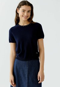 Marineblauer Strickpullover mit kurzen Ärmeln und Rundhalsauschnitt, verziert mit silbernen Akzenten am Kragen und Logodetail am Saum.