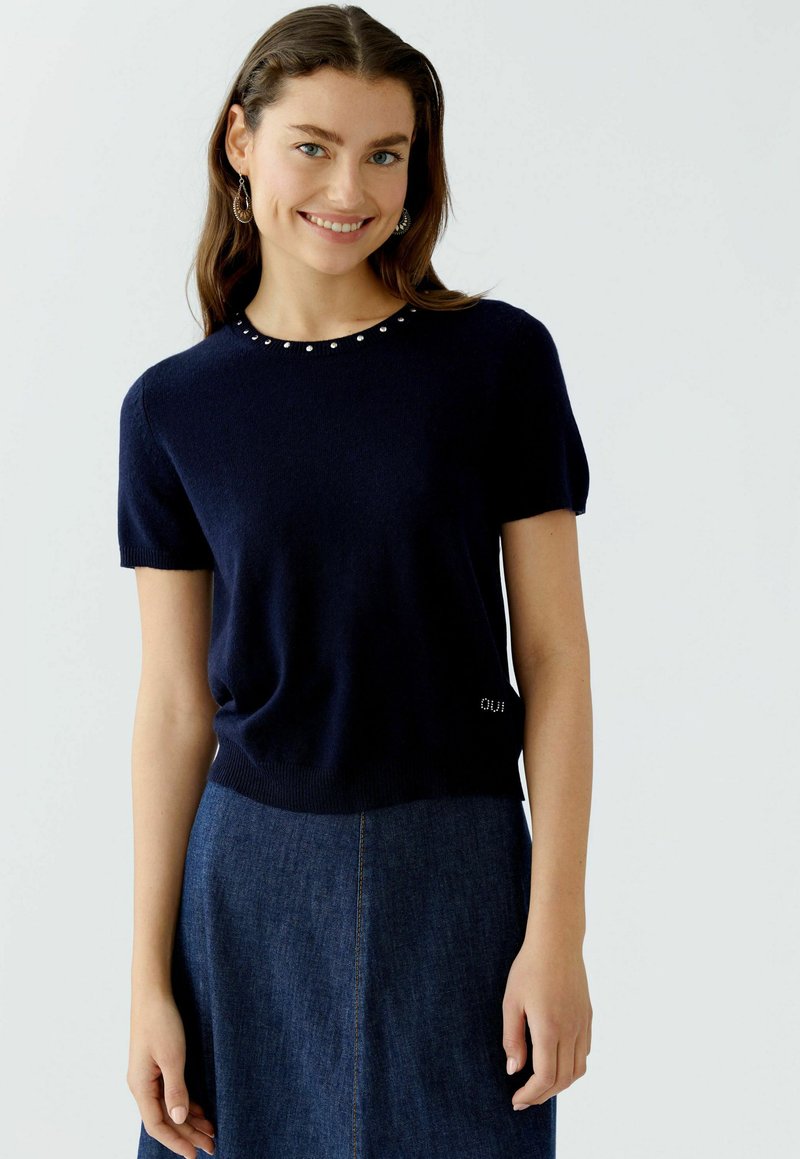 Marineblauer Strickpullover mit kurzen Ärmeln und Rundhalsauschnitt, verziert mit silbernen Akzenten am Kragen und Logodetail am Saum.