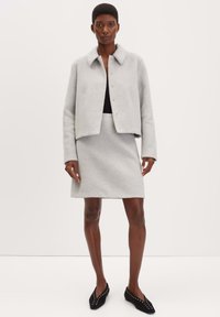 Grijze wollen blazer met een kraag en drukknoopsluiting, gecombineerd met een bijpassende grijze rok. Zwarte ballerina's met studs.