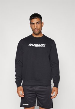 Zwarte sweatshirt met witte "HUMMEL" logo op de voorkant, lange mouwen en geribbelde manchetten. Draagt een bijpassende zwarte short.