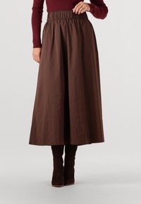 Bruine midi rok van gladde stof, met een elastische tailleband. Gecombineerd met bruin suède laarzen tot de knie. Netjes afgewerkte onderrand zonder patronen.