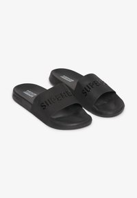Zwarte schuurlijke slippers van rubber, met een brede band met reliëftekst "SUPERDRY" en een getextureerde voetbed voor comfort.
