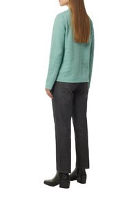 Aquamarinfarbener, strukturierten Mantel mit langen Ärmeln, kombiniert mit dunklen Jeans und schwarzen Stiefeletten, von hinten betrachtet.