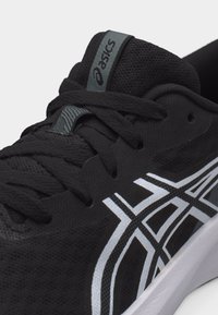 Κοντινό πλάνο μαύρου παπουτσιού τρεξίματος ASICS με μαύρα κορδόνια, υφασμάτινη πλέξη και λευκό λογότυπο στο πλάι, που δείχνει τη μαξιλαρωμένη γλώσσα με ετικέτα της μάρκας.