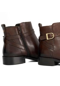 Brown leather ankle boots with a side zipper, featuring a buckle accent and smooth texture, in a rounded shape with a low heel.