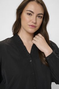 Camisa negra de botones con cuello con volantes, mangas largas con puños de botón y textura suave. Diseño elegante y minimalista.