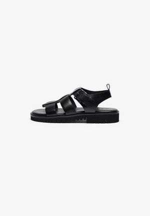 Black leather sandals with multiple straps, a buckle detail, flat sole, textured outsole, and a loop at the heel for easy wearing.