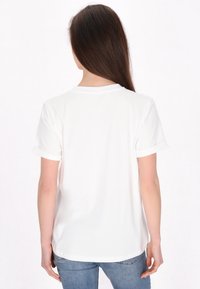 Witte t-shirt met korte mouwen en opgerolde manchetten, een ronde halslijn en een gladde textuur, vanuit de achterkant gezien tegen een egale achtergrond.