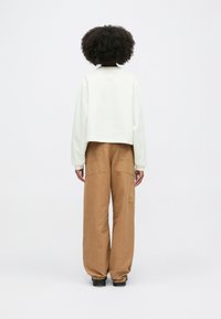 Κομμένο λευκό φούτερ με μακριά μανίκια σε συνδυασμό με καφέ παντελόνι cargo σε φάρδος, που διαθέτει πλαινά τσέπες και χαλαρή εφαρμογή.