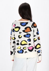 Pull en laine doux et blanc avec des motifs de cœurs et de formes colorés dans des teintes de bleu, rose, jaune, orange et des accents noirs ; poignets et col côtelés.