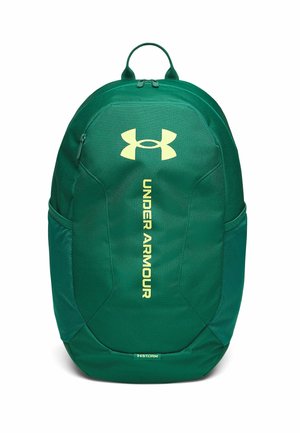 Groene Under Armour rugzak met bovenhandvat, voorvak met ritssluiting, zijvakken van mesh en verticale logo tekst op witte achtergrond.