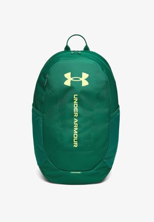 Zelený batoh Under Armour s horným madlom, predným vreckom na zips, bočnými sieťovanými vreckami a vertikálnym logom na bielom pozadí.