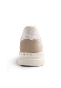 Sneaker di colore chiaro con tomaia in pelle bianca liscia e dettagli in suede beige, dotato di suola in gomma testurizzata e logo in rilievo.