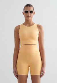 Lichtgele sportset bestaande uit een cropped tanktop met uitsnijding en high-waisted shorts, gemaakt van rekbare, gladde stof.