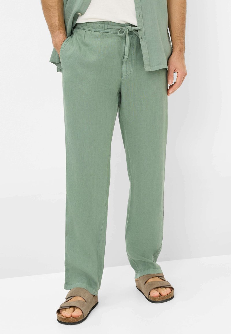 Light green linen trousers with a relaxed fit, elastic waistband, and drawstring detail, paired with brown flat sandals.