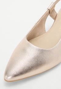 Gros plan d'une chaussure slingback beige métallique à bout pointu avec une texture lisse et un talon bas.