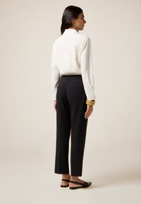 Witte blouse met lange mouwen en een kraag, gecombineerd met zwarte gepaste broek. Zwarte platte sandalen met een gesp. Glad stof en strakke lijnen.