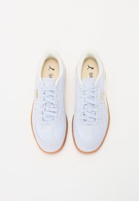 Ljusblå Puma-sneakers med gummisulor, vit innerfoder och snörning, visade uppifrån på en vit bakgrund.