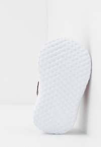 Schuhsohle mit einer welligen Textur, überwiegend weiß, mit pinkfarbenen Akzenten an den Kanten, entworfen für Halt und Traktion.