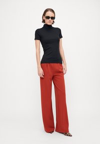 Maglione a collo alto nero a coste abbinato a pantaloni rossi a gamba larga a vita alta. Accessoriato con occhiali da sole scuri e scarpe a punta con stampa leopardata.