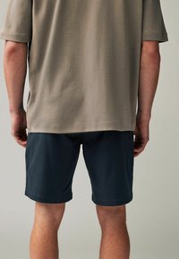 Camisa de algodón beige de manga corta, combinada con pantalones cortos azul marino oscuros. Presenta un corte relajado y un diseño sencillo, sin patrones ni acentos visibles.