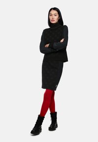 Schwarzer Pullover mit strukturiertem Muster, kombiniert mit einem dunklen Rock und roten Strumpfhosen. Abgerundet mit schwarzen Schnürstiefeln.