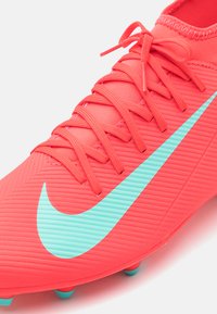 Crvena nogometna kopačka s teksturiranom površinom, koja ima veliki akvamarin Nike znak i odgovarajuće akvamarinske studove, uz crvene vezice.