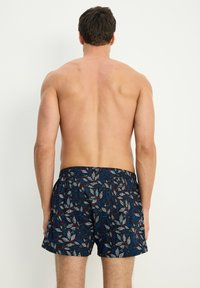 Männer Badehosen mit navy Hintergrund und einem Blattmuster in Grau, Rot und Blau. Elastischer Taillenbund, knielange Form, leichtes Material.