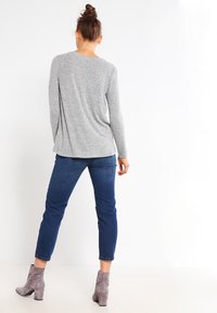 Haut gris à manches longues avec une coupe ample, associé à un jean bleu marine et des bottines grises. Texture lisse et design minimal.