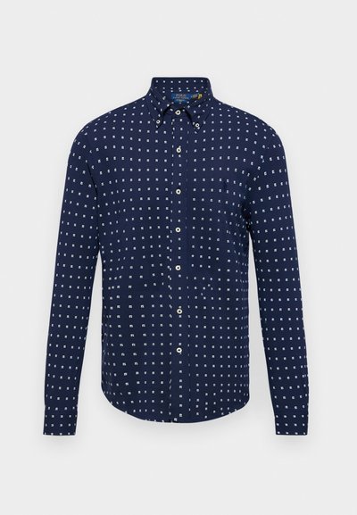 Jūrų mėlynos spalvos marškiniai su ilgomis rankovėmis, puoštomis baltų geometrinių kvadratų raštu, turi smailų kolorą. Pagaminti iš lengvos medvilnės audinio.