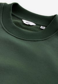 Grüner Sweatshirt mit geripptem Rundhalsausschnitt; aus einem weichen, strukturierten Material; Etikett im Kragen sichtbar.